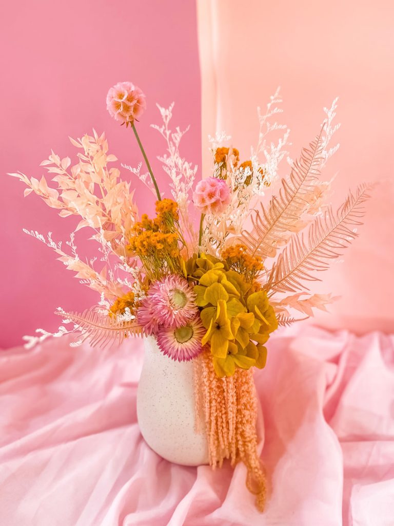 White textured vase with dried floral arrangement in warm pink, peach, white and yellow tones