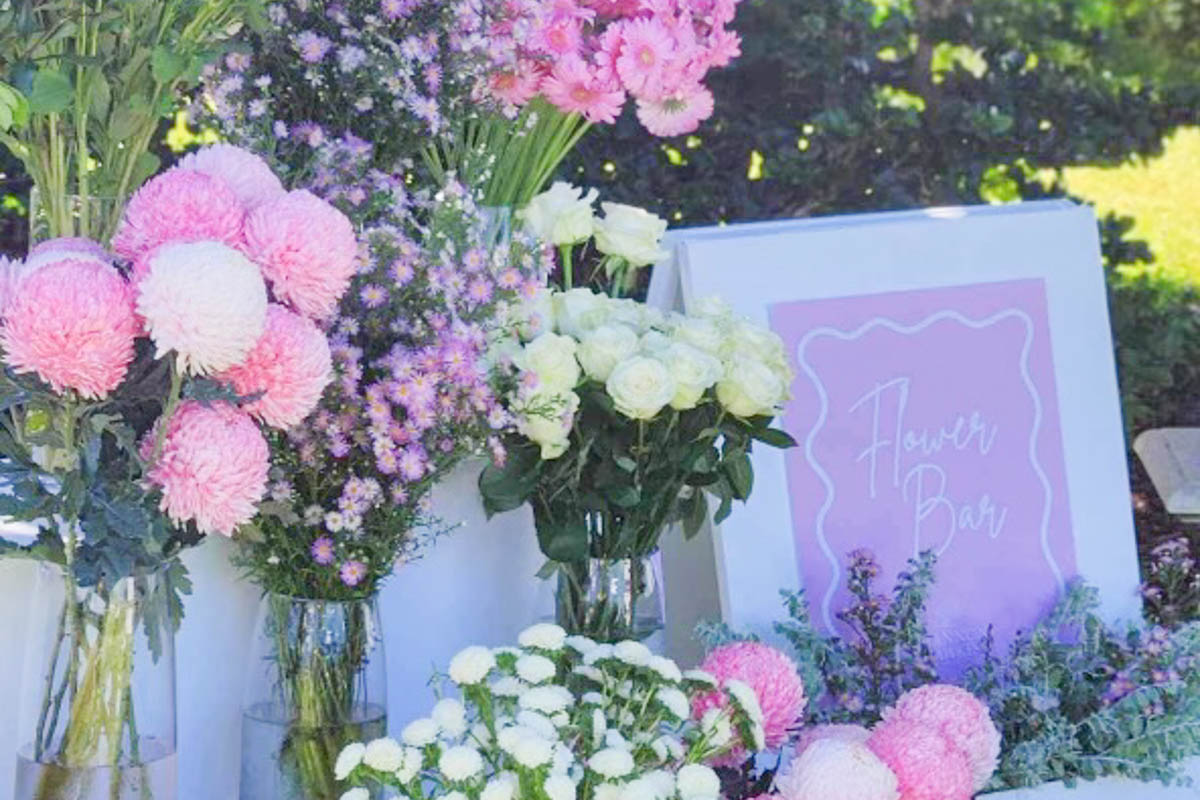 A flower bar with fresh flowers in shades of pink, cream and purple next to a sign that says 'flower bar'