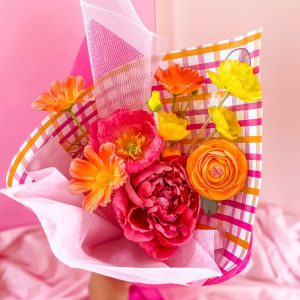 Bouquet of brightly coloured silk artificial flowers in pink, orange and yellow tones wrapped in paper and tied with ribbon