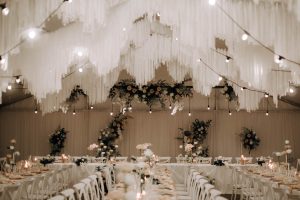Wedding reception ceiling installation with white fabric tassels, lights and flowers